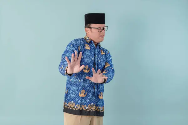 stock image Serious government worker man wearing blue batik uniform with hand gesture pose rejection or prohibition. PNS civil servant concept.