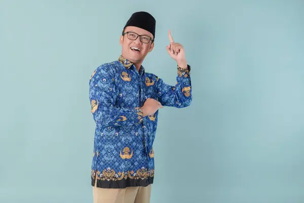 stock image Happy government worker man wearing blue batik uniform pointing to the copy space upward. PNS civil servant concept.