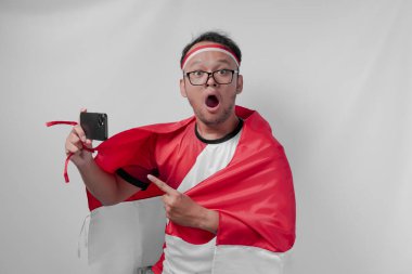 Çekici Endonezyalı adam forma giyip omzunun üstünde bayrak sallayarak telefonla spor müsabakalarını izliyor. Endonezya Bağımsızlık Günü kavramı.