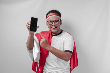 Forma giyen mutlu Endonezyalı adam beyaz arka plan üzerinden telefonunu işaret ediyor. Endonezya Bağımsızlık Günü ve spor konsepti.