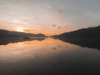 Sermo Gölü, Yogyakarta, Endonezya 'da günbatımının hava görüntüsü, berrak suyun üzerinde güneş yansımaları var..