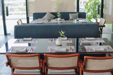 Bir restoranda yemek için içinde yeşil bitki ve gümüş vazo bulunan siyah bir yemek masası hazırlanıyor..