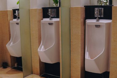 Halka açık bir tuvalette, aralarında bir bölme olan üç beyaz pisuvar sıraya dizildi..