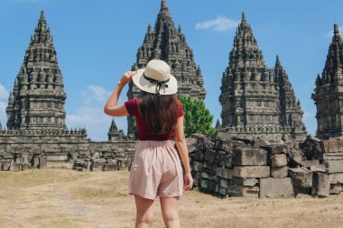 Back portrait of a young Indonesian woman wearing a straw hat enjoying the view of Prambanan temple in Yogyakarta. Holiday and travel concept.