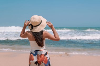 Back portrait of a young Indonesian woman wearing a straw hat enjoying the view of Drini beach in Yogyakarta. Holiday and travel concept.