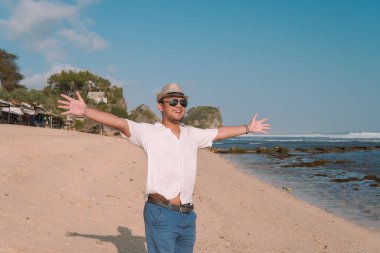 Back portrait of an excited young Asian man wearing a straw hat stands by Drini beach in Yogyakarta, Indonesia. Holiday and travel concept.