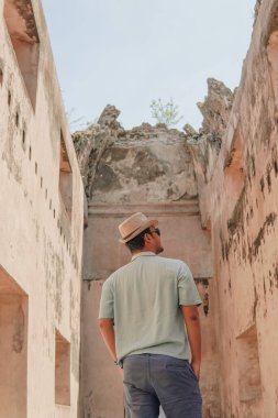 Back portrait of a young Indonesian man wearing a hat enjoying the view of Tamansari in Yogyakarta, holiday and travel concept.