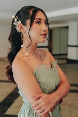 Chic young Asian woman in a green dress and a flowery accessory is posing for a photo.