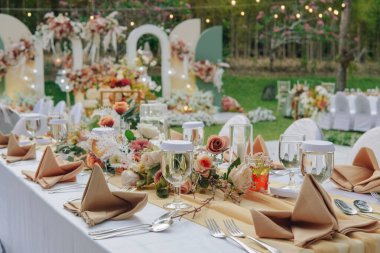 Beyaz masa örtüsü ve ortasında zarif bir çiçek aranjmanı olan uzun masa, bir düğün ya da özel bir etkinlik için hazırlanır..