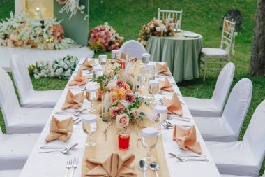 Beyaz masa örtüsü ve ortasında zarif bir çiçek aranjmanı olan uzun masa, bir düğün ya da özel bir etkinlik için hazırlanır..