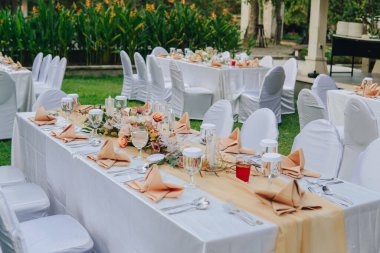 Beyaz masa örtüsü ve ortasında zarif bir çiçek aranjmanı olan uzun masa, bir düğün ya da özel bir etkinlik için hazırlanır..