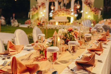Beyaz masa örtüsü ve ortasında zarif bir çiçek aranjmanı olan uzun bir akşam yemeği masası, bir düğün ya da özel bir etkinlik için hazırlanır..