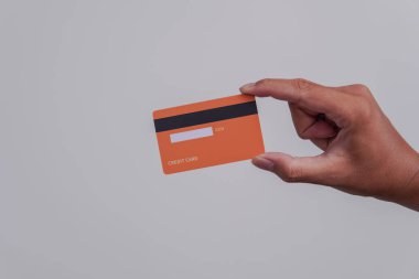 Person's hand showing the back of a credit card or debit card with orange color over isolated white background.