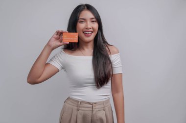 Gorgeous young Asian woman wearing casual attire presenting a credit card, isolated by white background.