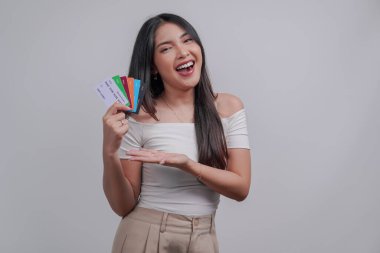 Excited young Asian woman presenting credit cards or debit cards, isolated by white background.