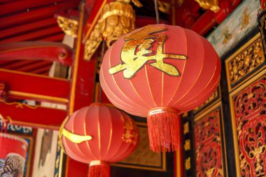 The red lanterns hanging from the temple or klenteng ceiling have gold accents and Chinese characters on them.