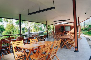 Yeşil bahçedeki büyük çadırın altında masa ve sandalyeler olan açık hava kafeteryası ya da yemek salonu..