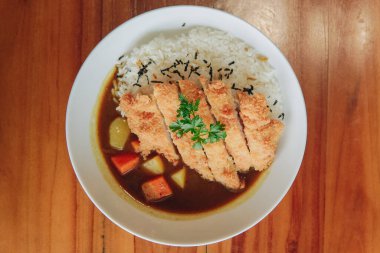 Japon körili pirinç ve patates ve havuçlu tavuk katsusu ahşap bir masada beyaz bir tabakta servis ediliyor..