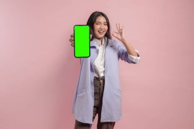 Heyecanlı genç Asyalı kadın telefon ekranında pembe arka planla izole edilmiş fotokopi çekerken iyi işareti gösteriyor..