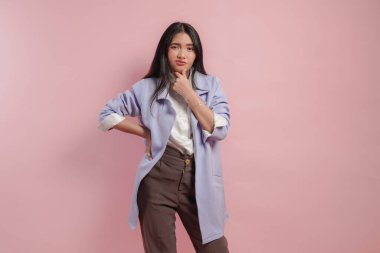 Mor paltolu düşünceli genç Asyalı kadın pembe arka planda izole edilmiş ciddi ifadeli bir fikir düşünüyor..