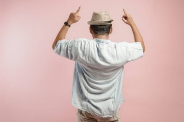 Şapkalı ve mavi gömlekli genç bir Asyalı 'nın arka portresi fotokopi alanını yukarıya doğru gösteriyor, pembe arka planda izole edilmiş..