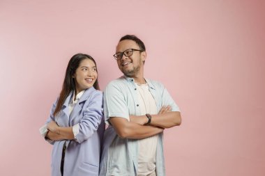 Confident young Asian couple smiling and posing with arms folded isolated over pink background.
