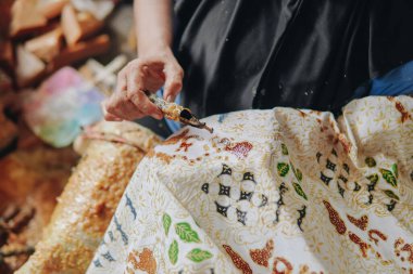 Close up picture of a person's hand drawing the design pattern of Indonesian batik tulis fabric using Canting and malam wax.