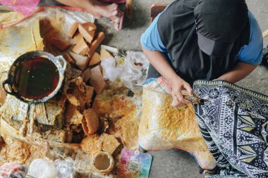 Top view of a woman drawing the colorful design pattern of Indonesian batik tulis fabric using Canting and malam wax.