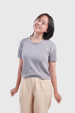 Attractive young Asian woman wearing gray shirt is standing and smiling to the camera isolated over white background.