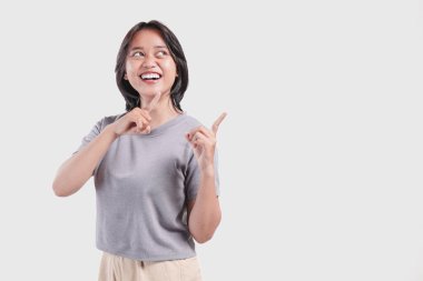Joyful young Asian woman presenting and pointing to the copy space beside her over isolated white background.
