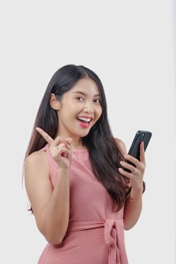 Arkasındaki fotokopi alanını işaret ederken akıllı telefon kullanan pembe elbiseli güzel Asyalı kadın beyaz arka planla izole edilmiş..