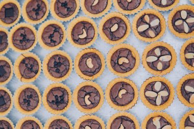 Bir tepsi mini brownie tartlet. Üstünde fındık ve çikolata parçacıklı kek..