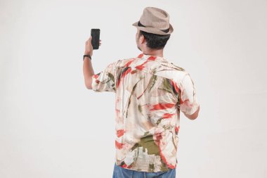 Hawaii tişörtü giyen genç bir Asyalı 'nın arka portresi. Video görüşmesi için akıllı telefon kullanıyor, beyaz arka planda izole edilmiş..