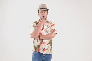 Havai gömleği ve şapkası giyen düşünceli Asyalı genç adam beyaz arka planda izole edilmiş ciddi bir yüz ifadesi olan bir fikir düşünüyor..