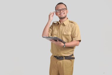 Calm Indonesian government worker man wearing khaki uniform holding document paper and smiling to the camera. PNS civil servant concept.
