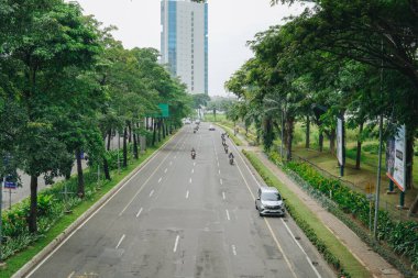 Arka planda yüksek bina olan şehir yolu, yolda ilerleyen birkaç araç..