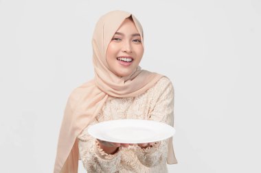 Güzel Asyalı genç Müslüman kadın tesettürde boş bir tabakta fotokopi alanı sunuyor, iftar için yemek menüsünü gösteriyor.