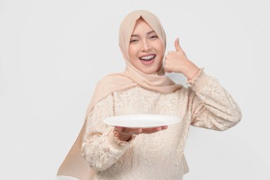 Heyecanlı genç Asyalı tesettürlü Müslüman kadın boş beyaz plaka fotokopi alanını sunarken başparmak hareketi yapıyor..