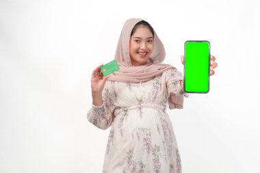 Gülümseyen Asyalı hamile kadın akıllı telefonunda kopya alanı ve beyaz arka planda izole edilmiş kredi veya banka kartını sunuyor..