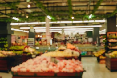 Blurry image of a grocery store with a lot of fruit and vegetables. Scene is busy and bustling, with people shopping.