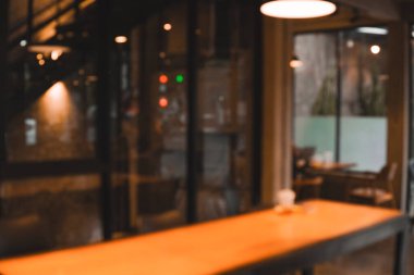 Loş ışıklandırmalı masa ve sandalye dolu bir kafenin bulanık görüntüsü.