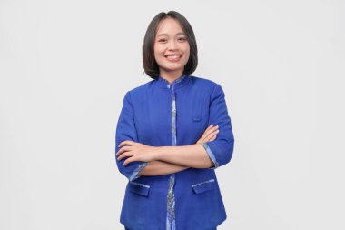 Confident Asian customer service woman wearing blue uniform standing with arms folded, isolated over white background.
