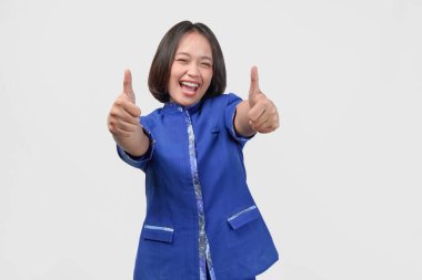 Cheerful Asian customer service woman in blue uniform gesturing thumb up of approval, isolated by white background.