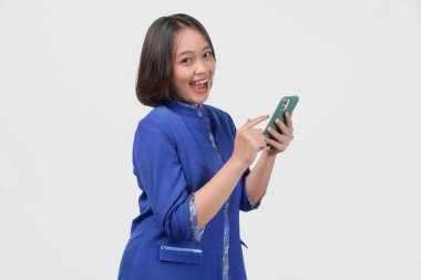 Smiling Asian customer service woman in blue uniform using smartphone with happy expression, isolated over white background.
