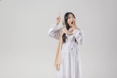 Tesettürlü hamile Asya 'lı hamile kadın, beyaz arka planla izole edilmiş kopya alanını işaret ediyor. Ramazan kavramı.