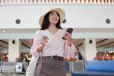 Excited young Asian woman smiling while holding a ticket and a smartphone to go on a holiday.