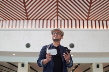 Excited young Asian man bringing backpack smiling while holding a ticket and a smartphone to go on a holiday.