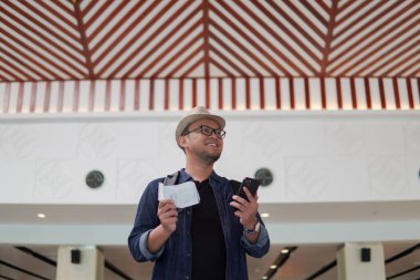 Excited young Asian man bringing backpack smiling while holding a ticket and a smartphone to go on a holiday.