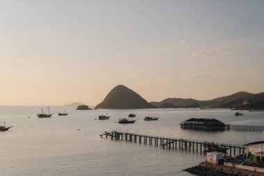 Beautiful scenery of tropical island harbor with long bridge pier and boats in Labuan Bajo, Indonesia.