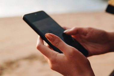 Close up of a woman's hand holding and using a smartphone while enjoying holiday in Waecicu Beach, Labuan Bajo.